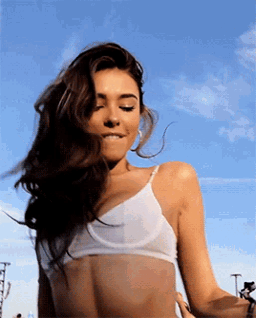 a woman in a white bra stands in front of a blue sky with clouds