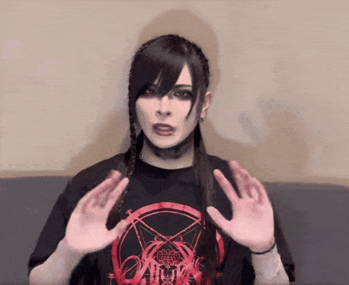 a woman wearing a black shirt with a pentagram on it holds her hands up