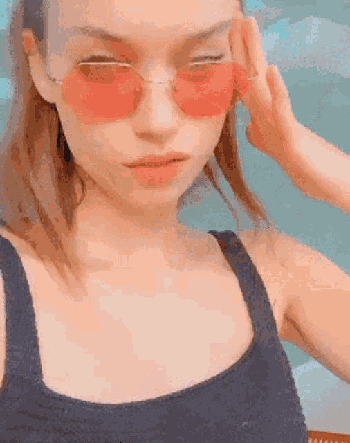 a woman wearing red sunglasses and a black tank top takes a selfie