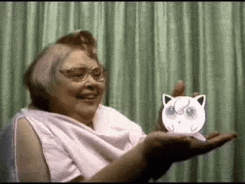 an elderly woman is holding a paper cut out of a cat in her hands .