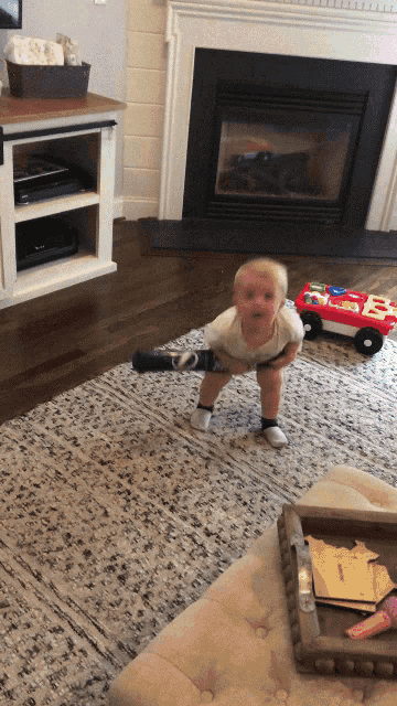 a baby is standing on a rug in front of a fireplace holding a toy that says e on it