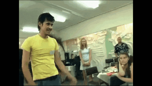 a man in a yellow shirt is dancing in front of a group of people .
