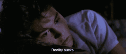 a man is laying in bed with his eyes closed and the words reality sucks .
