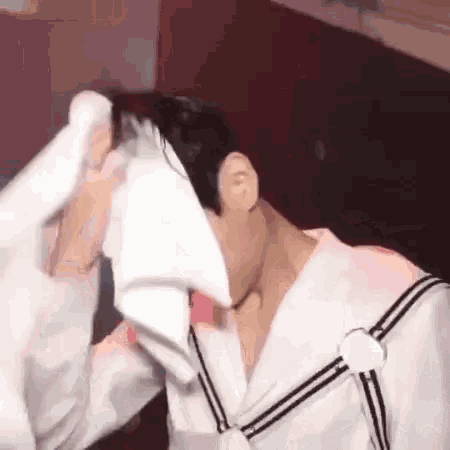 a man in a sailor suit is wiping his face with a white towel .