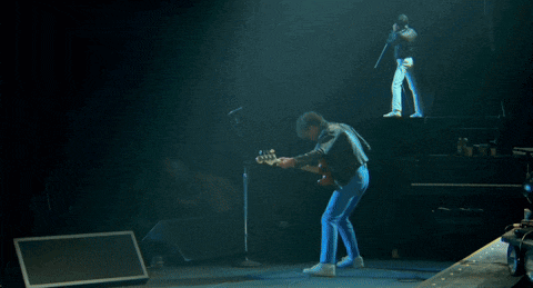 a man playing a guitar on stage with a drum set in the background