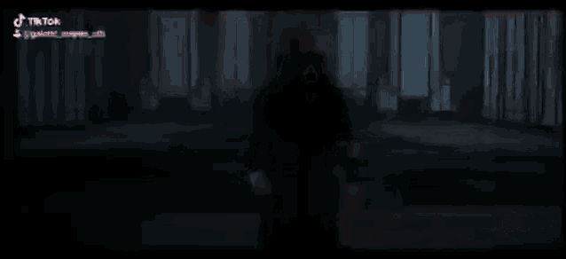 a man in a hooded robe is holding two red lightsabers in a dark room .