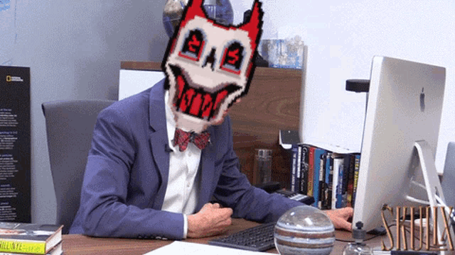 a man in a suit and bow tie sits at a desk with a computer and a national geographic book