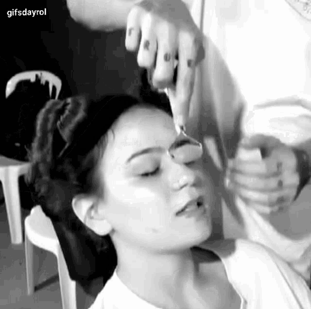 a black and white photo of a woman getting her eyebrows shaved by a man .