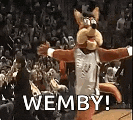 a mascot is dancing in front of a crowd at a basketball game and says wemby .