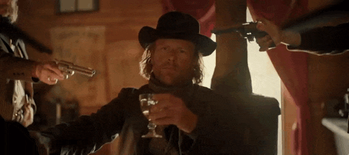 a man in a cowboy hat is holding a glass of whiskey and a gun
