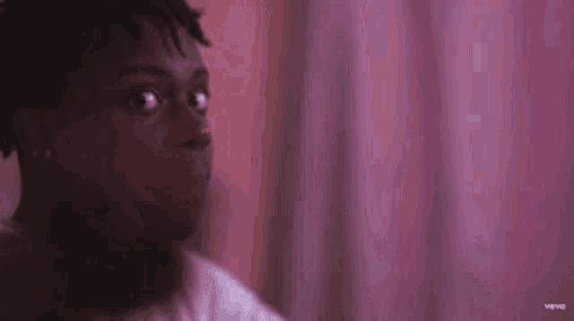 a young man is sitting in front of a pink curtain and looking at the camera .