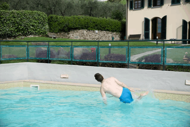 a man is jumping into a pool with a house in the background