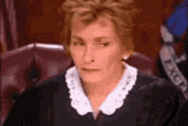 a judge is sitting in a courtroom wearing a black robe and white collar .