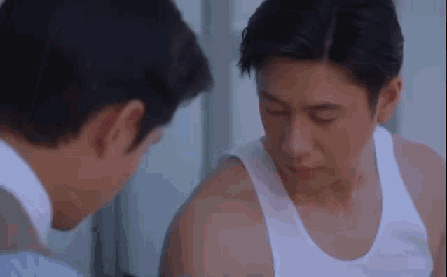 a man in a white tank top is looking at another man 's shoulder .