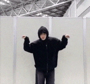 a man in a black jacket with a hood is standing in front of a wall .