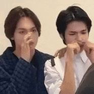 two young men are sitting next to each other and one of them is covering his mouth .