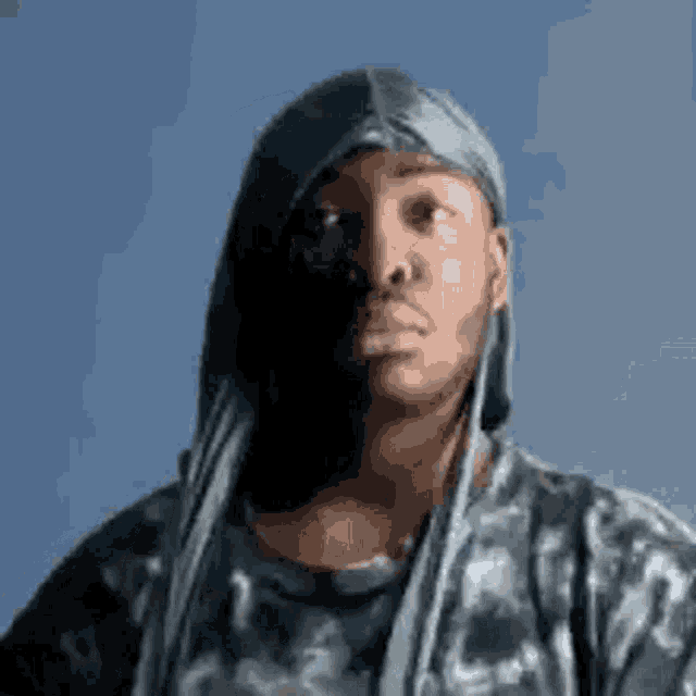 a man wearing a head scarf and a t-shirt is looking at the camera .