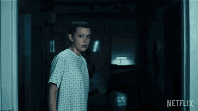a girl in a hospital gown is standing in a dark hallway with a netflix logo in the corner