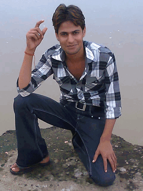 a young man in a plaid shirt is kneeling on a rock