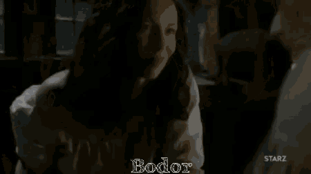 a man and a woman are standing next to each other in a dark room with the word bodor on the bottom .