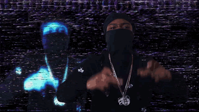 a man wearing a black turtleneck and a necklace with a coin on it stands in front of a purple wall