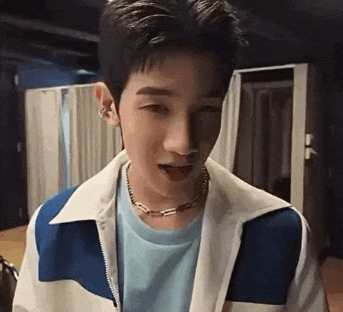 a young man wearing a blue and white jacket and a necklace is sticking out his tongue .