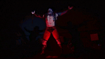 a wrestler is standing in a dark room with his arms outstretched in the air .