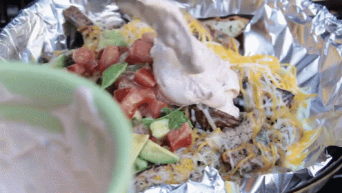 a close up of a foil packet of nachos with tomatoes , cheese and avocado .