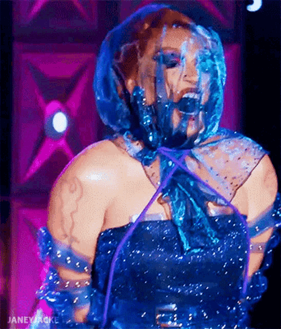 a woman in a blue dress with a plastic bag over her head is dancing on a stage .