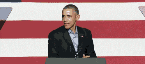 a man in a suit stands at a podium in front of an american flag