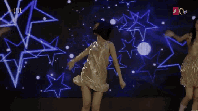 a woman in a gold dress is dancing in front of a screen that says " live "