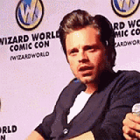 a man is sitting in front of a sign that says wizard world comic con on it .