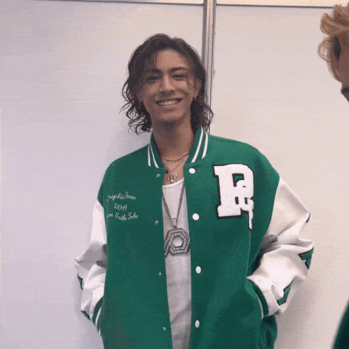 a man wearing a green and white varsity jacket with the letter r on the sleeve