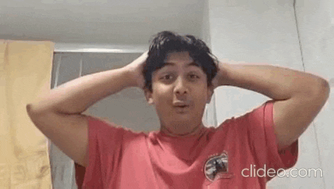 a young man in a red t-shirt is holding his head in his hands .