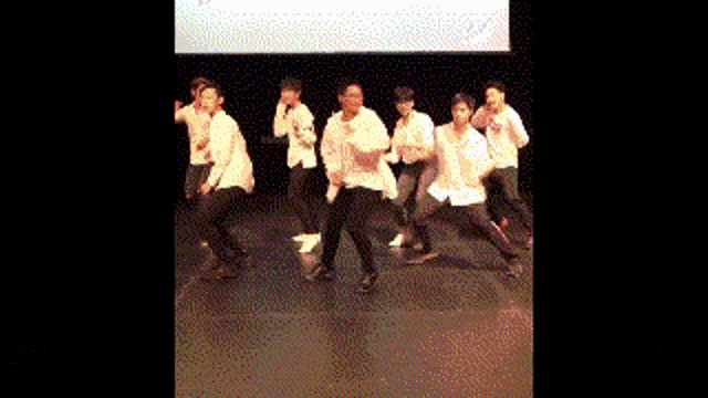a group of young men are dancing on a stage in front of a large screen .