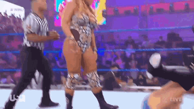 a woman is standing in a wrestling ring while a referee stands behind her .