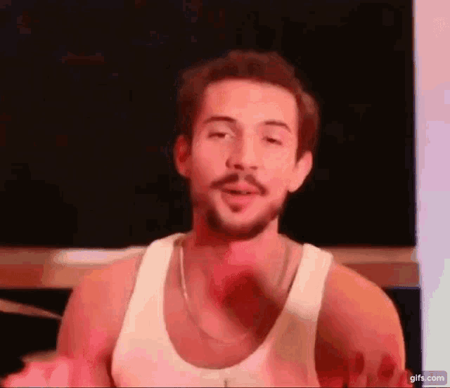 a man with a beard and a white tank top is making a funny face .