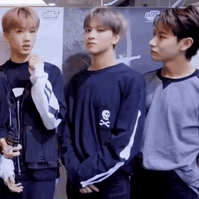 three young men are standing next to each other and one of them has a blue shirt with a skull and crossbones on it
