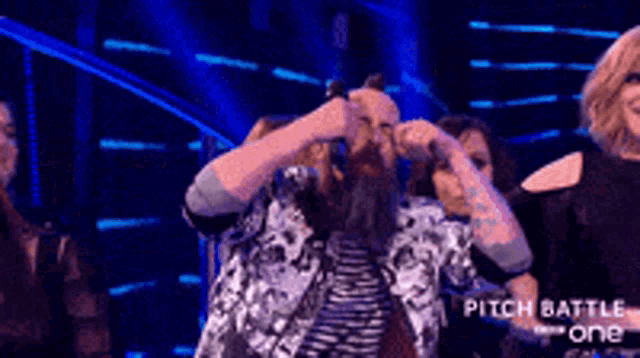 a man with a beard is singing into a microphone on a stage in front of a group of people .