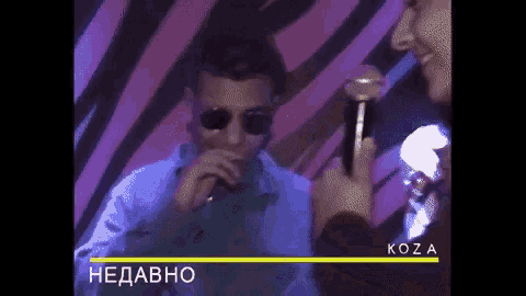 a man wearing sunglasses is singing into a microphone while another man takes a picture of him .