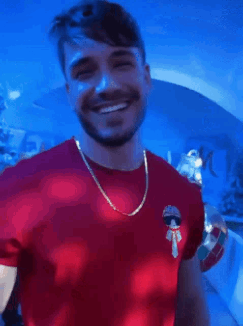 a man with a beard is wearing a red shirt and a gold chain around his neck