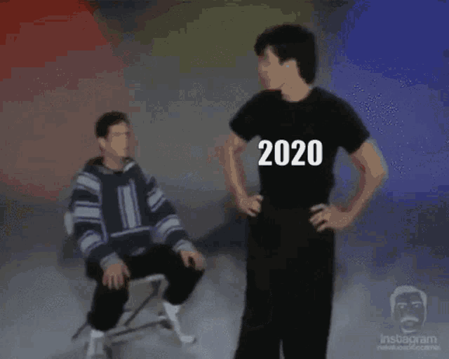 two men are standing next to each other and one of them is sitting in a chair and the other is standing and says 2020