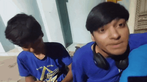 a boy wearing a blue shirt that says trademark is sitting next to another boy wearing headphones