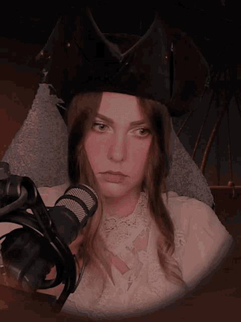 a woman wearing a pirate hat and a white shirt stands in front of a microphone