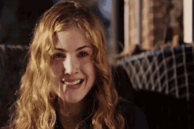 a woman with long blonde hair is smiling and looking at the camera while sitting on a couch .