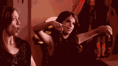two women are sitting next to each other in a dark room and one of them is pointing at the camera .