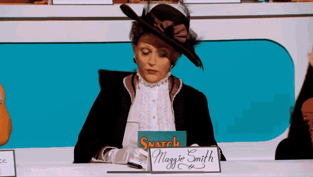 a woman in a hat sits at a desk with a sign that says snatch maggie smith