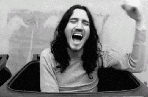 a black and white photo of a man with long hair sitting in a trash can .