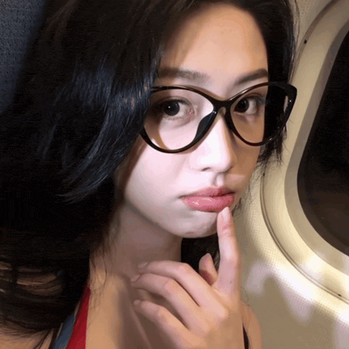 a woman wearing glasses has her finger to her mouth