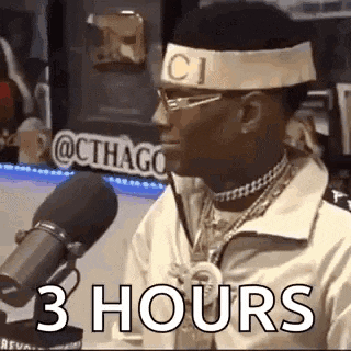 a man wearing a headband and glasses is sitting in front of a microphone and saying `` 3 hours '' .